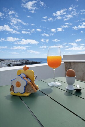 Ein Tisch mit Frühstücksangeboten und einem Glas Orangensaft mit Blick auf einen Strand.