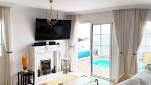 A living room with a sofa, a glass coffee table, a fireplace, a TV, and a view of the pool. - Villa with sea views and private pool overlooking the harbour. (Tías)
