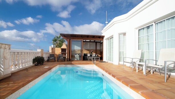 A swimming pool with a patio area, a covered seating area, and a view of a building with large windows. - Villa with sea views and private pool overlooking the harbour. (Tías)