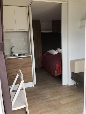 A compact room with a kitchenette, a bed with a red blanket, and a small seating area.