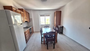 A kitchen with wooden cabinets, a white refrigerator, a dining table with chairs, and a window with blinds. - Seafront apartment in Santa Maria di Castellabate near the Pepi Promenade (Santa Maria di Castellabate)