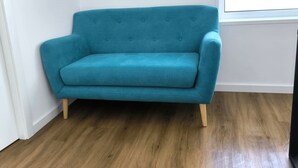 A teal sofa in a room with wooden flooring and a white wall. - Loreto Apartment (Bragança)