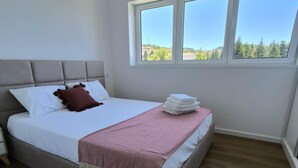 A bedroom with a bed, a window, and a view of greenery. - Loreto Apartment (Bragança)