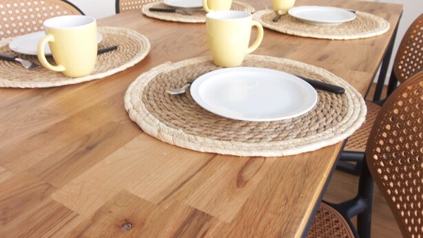 A wooden dining table with yellow mugs and white plates on woven placemats. - Loreto Apartment (Bragança)