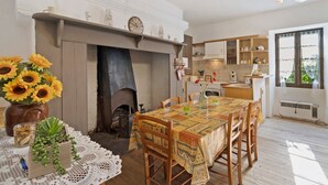 A dining area with a fireplace, wooden table, chairs, and a view of the kitchen. - Holiday Home "Le Pigeonnier" with Private Pool (Saint-Pompon)