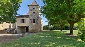 A stone building with a tower, a grassy yard, and a bench. - Holiday Home "Le Pigeonnier" with Private Pool (Saint-Pompon)