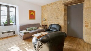 A living room with a stone wall, a sofa, a leather chair, a wooden coffee table, and a door. - Holiday Home "Le Pigeonnier" with Private Pool (Saint-Pompon)