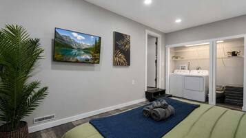 A bedroom with a bed, a potted plant, a painting, a washing machine, and a dryer.