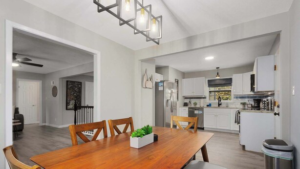 A modern kitchen with white cabinets, a stainless steel refrigerator, and a dining area with a wooden table and chairs.