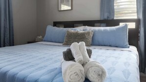 A neatly made bed with rolled towels, a headboard, and a framed picture on the wall.