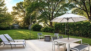An outdoor patio with a table and chairs, a small round table, and a large umbrella.