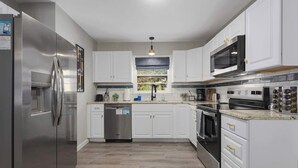 A modern kitchen with stainless steel appliances, white cabinetry, and a wooden floor.