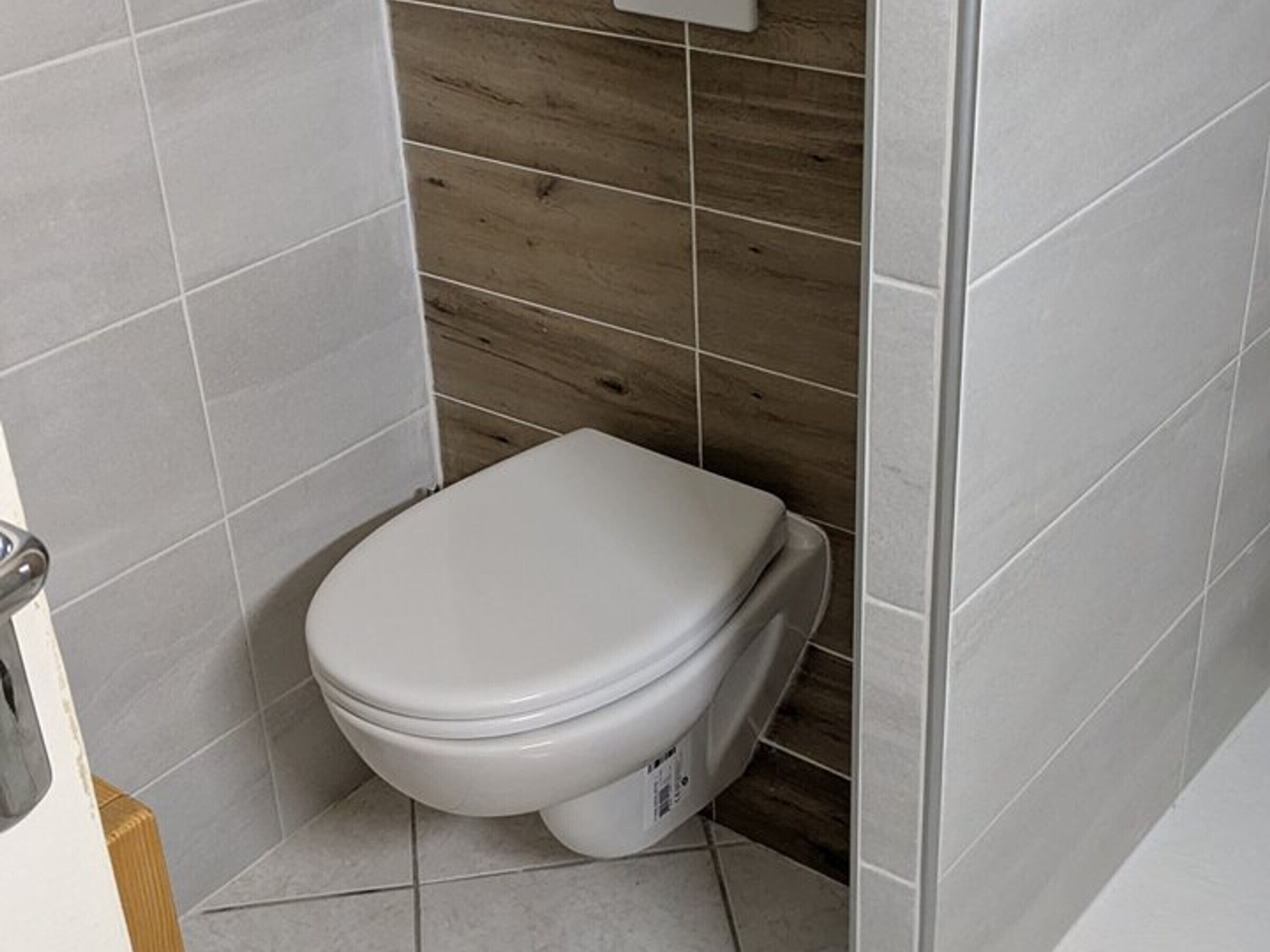Une petite salle de bain moderne avec des toilettes blanches, des murs carrelés et un mur d’accent en bois.