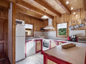 A kitchen with wooden walls, a white refrigerator, a stove, and a sink. There are hanging pots and a coffee maker on the counter.