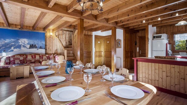 Een houten eetgedeelte met een grote tafel voor zes personen, een trap en een keuken met een koelkast.