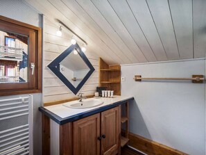 Une salle de bain avec un meuble-lavabo en bois, un miroir avec éclairage intégré, un porte-serviettes et une fenêtre donnant sur l’extérieur.