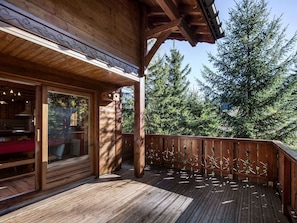 A wooden deck with a glass door leading to a room, surrounded by trees.