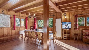 Interieur van een houten hutje met een eethoek, een televisie en een groot raam.