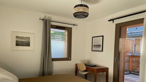 Una camera da letto con un letto, una scrivania e una sedia. Si vede una finestra con tende, un quadro appeso al muro e una porta che dà su uno spazio esterno.