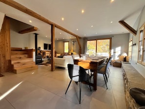 A spacious living area with a wooden staircase, a dining table set for four, and a large window offering a view of the outdoors. - Renovated chalet in Samoëns, near center, ski bus (Samoëns)