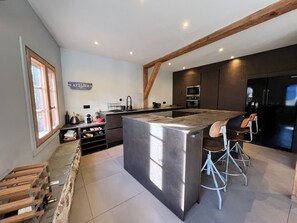 A modern kitchen with a large island, dark cabinetry, and a wooden ceiling beam. - Renovated chalet in Samoëns, near center, ski bus (Samoëns)