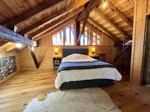 A cozy attic bedroom with a wooden ceiling, a large bed, two bedside tables with lamps, and a stone wall. - Renovated chalet in Samoëns, near center, ski bus (Samoëns)