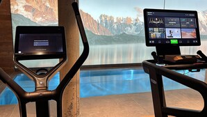 Un gimnasio con equipo de ejercicio, un ventanal con vistas a la montaña y una pantalla digital en el equipo.