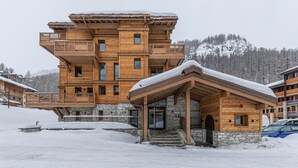 Un edificio de madera de varios pisos con balcones y un cimiento de piedra, rodeado de nieve.