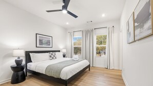 Quarto moderno com cama, duas mesas de cabeceira, ventilador de teto e janela com cortinas.