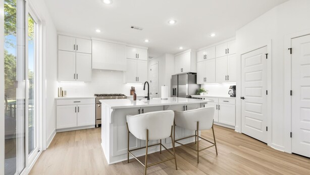 Cozinha moderna com armários brancos, uma ilha central com banquetas e uma janela grande que proporciona iluminação natural.