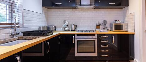 A modern kitchen with a wooden countertop, stainless steel appliances, and black cabinetry.