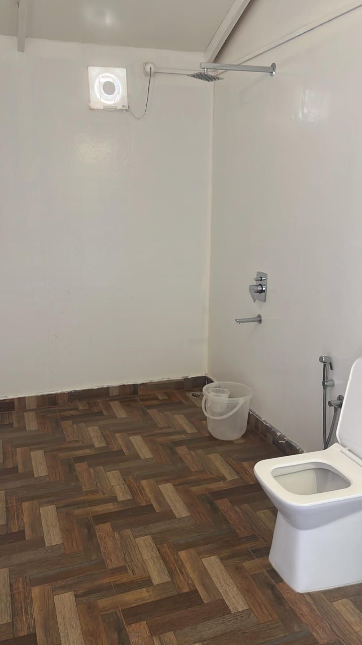 Ein Badezimmer mit Holzboden, Toilette, Dusche und einer Wandleuchte.