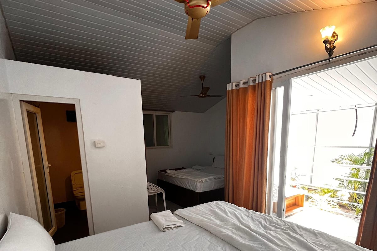 A hotel room with a bed, a ceiling fan, a window with curtains, and a view of the outside.