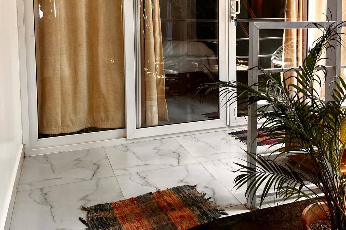 A sliding glass door leading to a balcony with a potted plant and a woven mat.