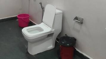 A small, enclosed bathroom with a toilet, a shower, and a trash bin.