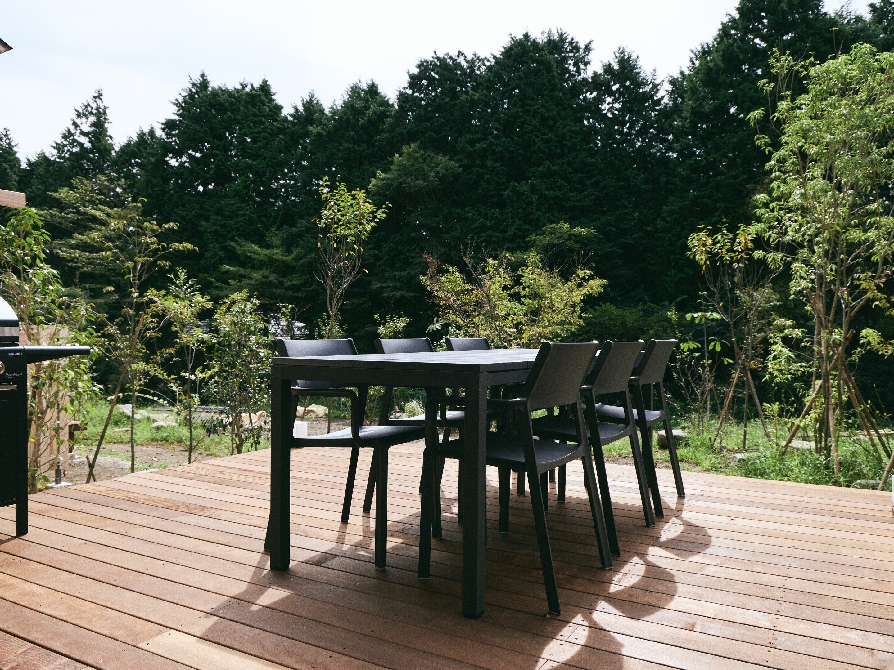 A wooden deck with a table and chairs, surrounded by trees.