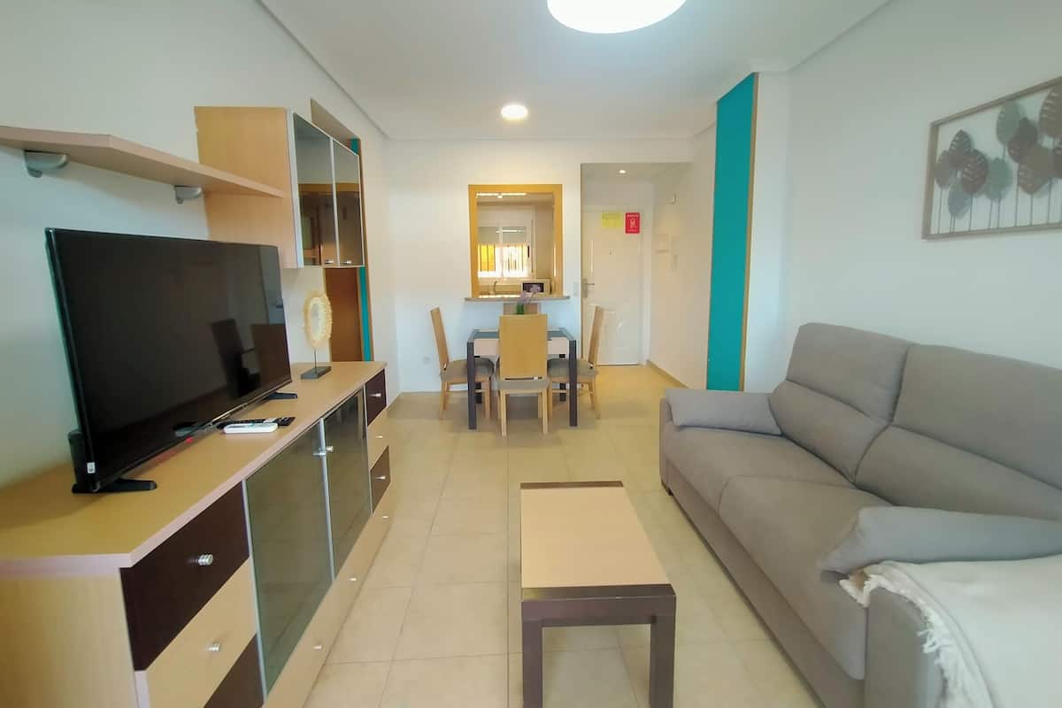 Een moderne woonkamer met een flatscreen televisie, een bank, een salontafel en een eethoek met stoelen en een tafel.