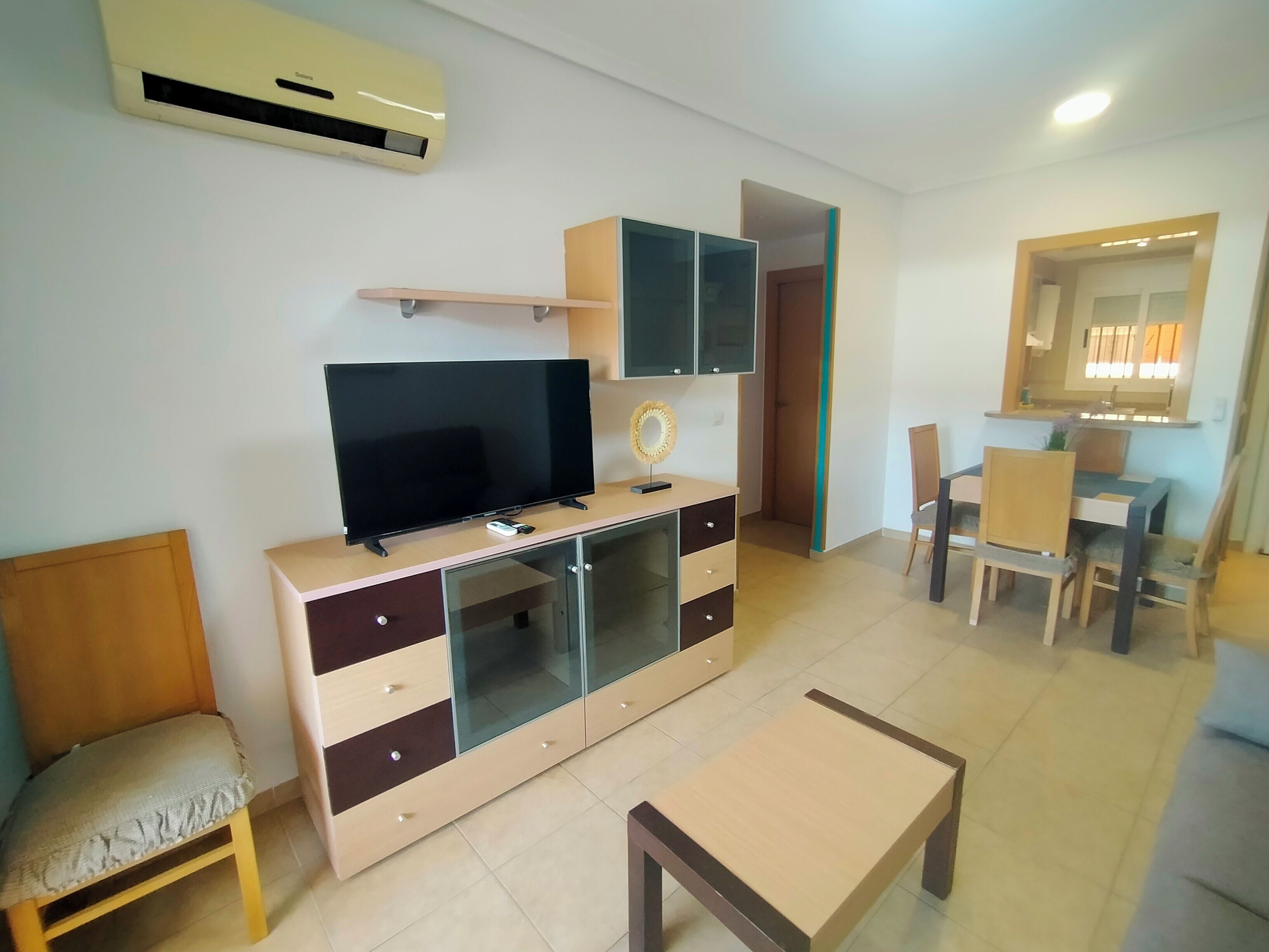 A living room with a flat-screen TV on a wooden cabinet, a small table, and a dining area with chairs and a table.