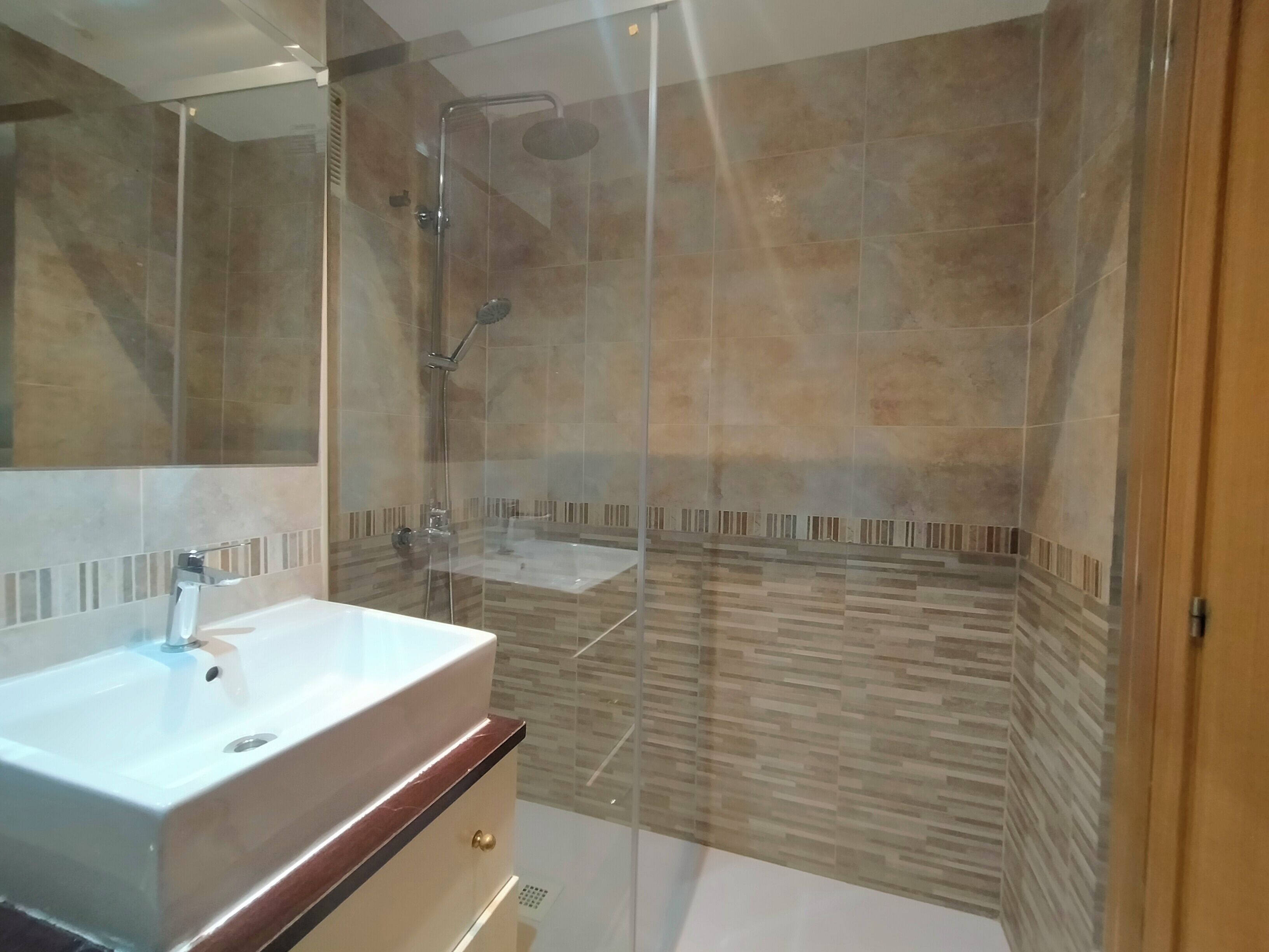 Ein modernes Badezimmer mit einer Duschkabine, einem weißen Waschbecken und einem Spiegel.