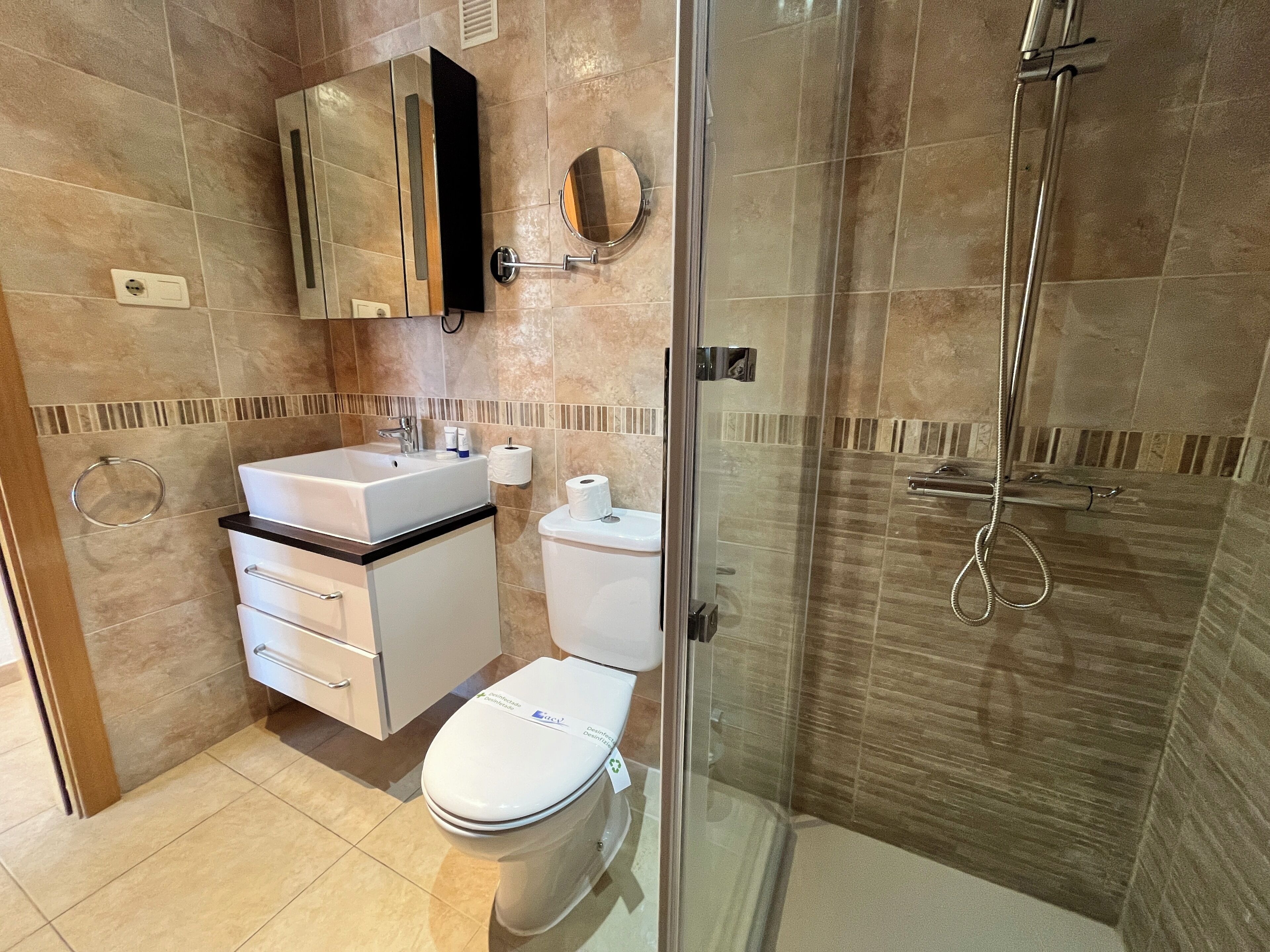 Un baño moderno con cabina de ducha de vidrio, un lavamanos blanco y un inodoro.