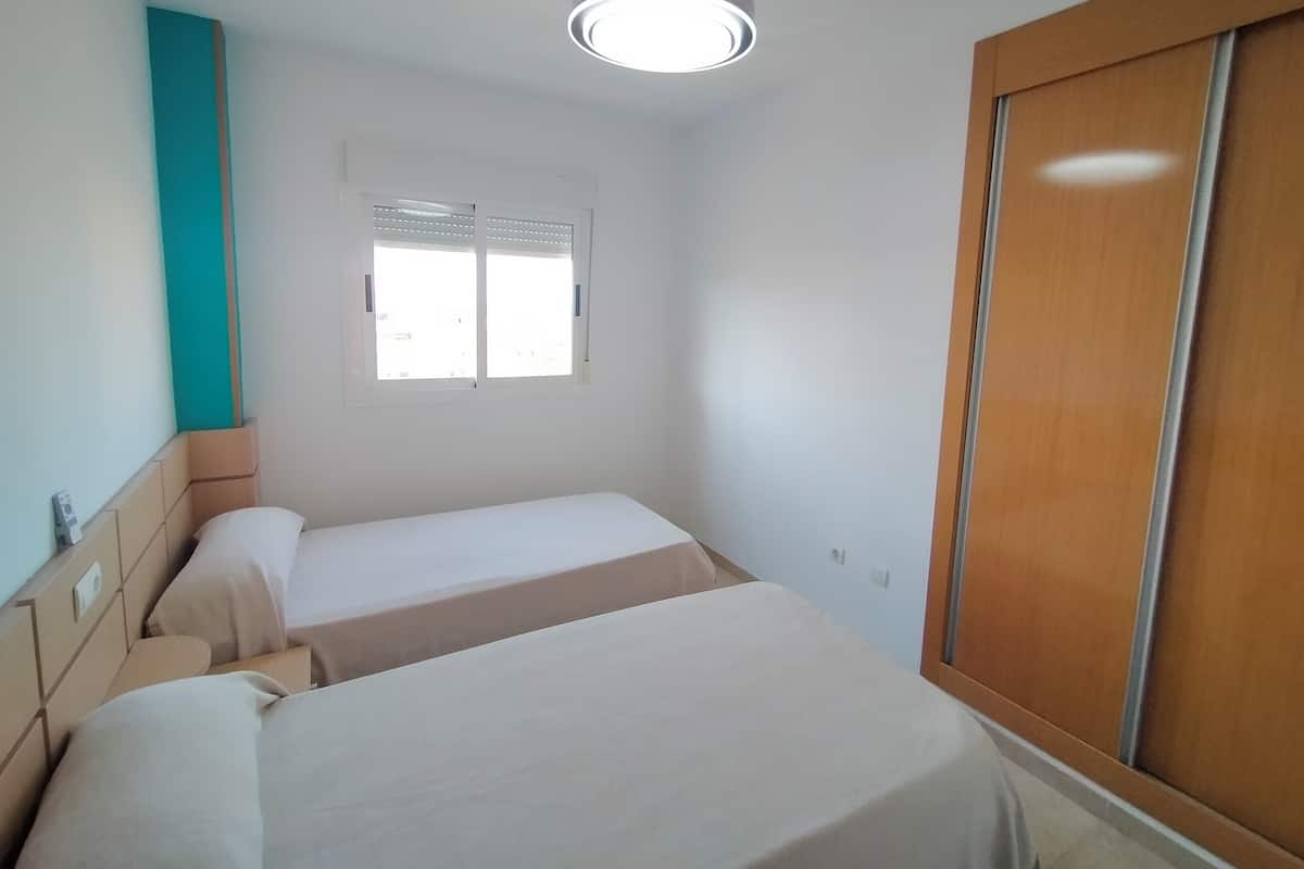 Een slaapkamer met twee bedden, een raam, een kledingkast en een plafondlamp.