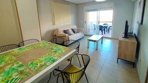 A dining area with a table and chairs, a sofa, a television, and a sliding glass door leading to an outdoor patio. - ACV - Apartamentos Torremar (Oropesa del Mar)