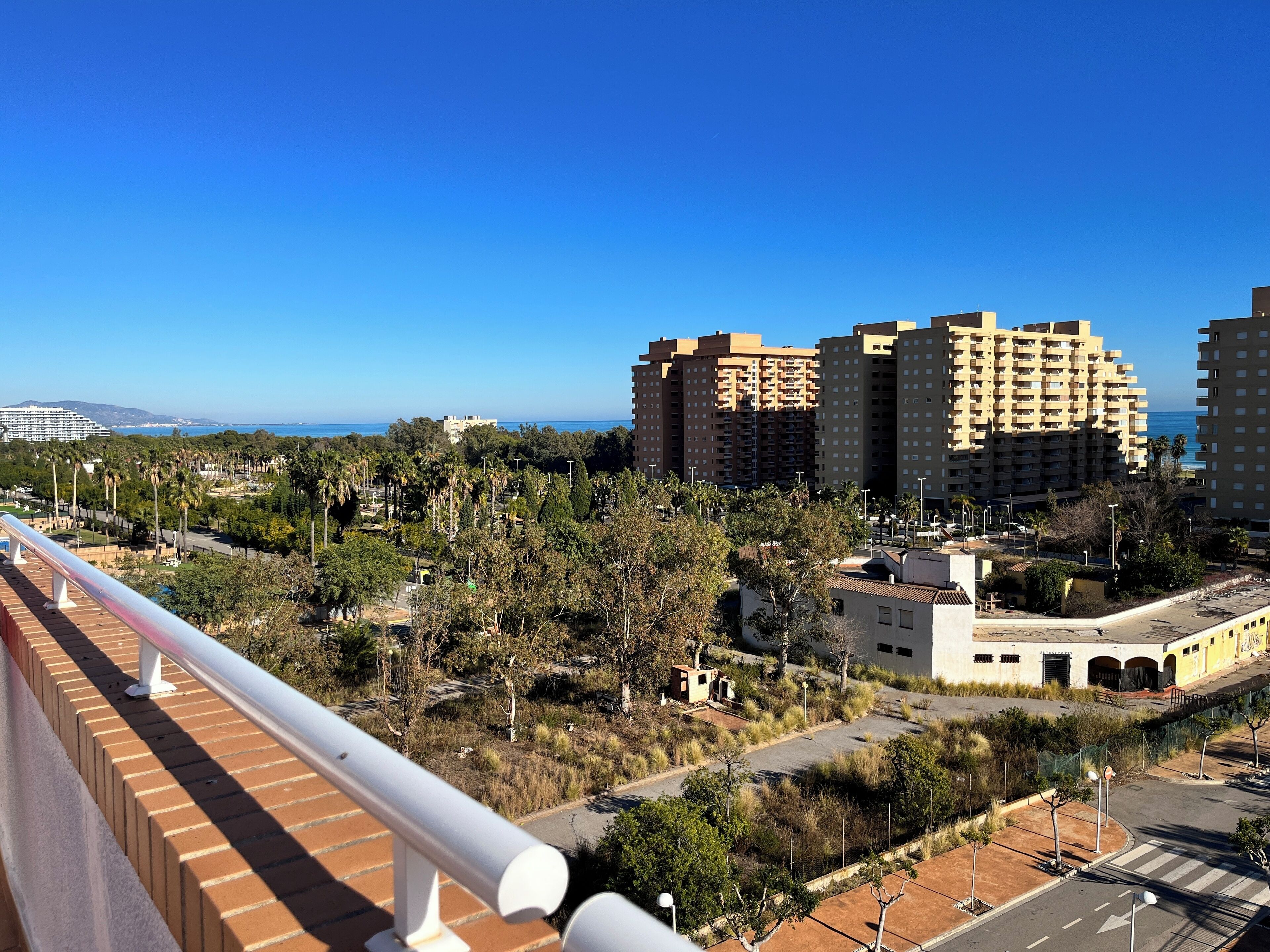 Un paisaje urbano costero con rascacielos, cielo azul despejado y vista al mar.