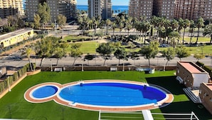 A residential area with a large swimming pool surrounded by green lawns and palm trees. - ACV - Apartamentos Torremar (Oropesa del Mar)