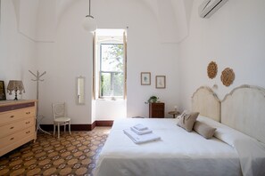 Een slaapkamer met een bed, een stoel, een dressoir, een raam en wanddecoraties.