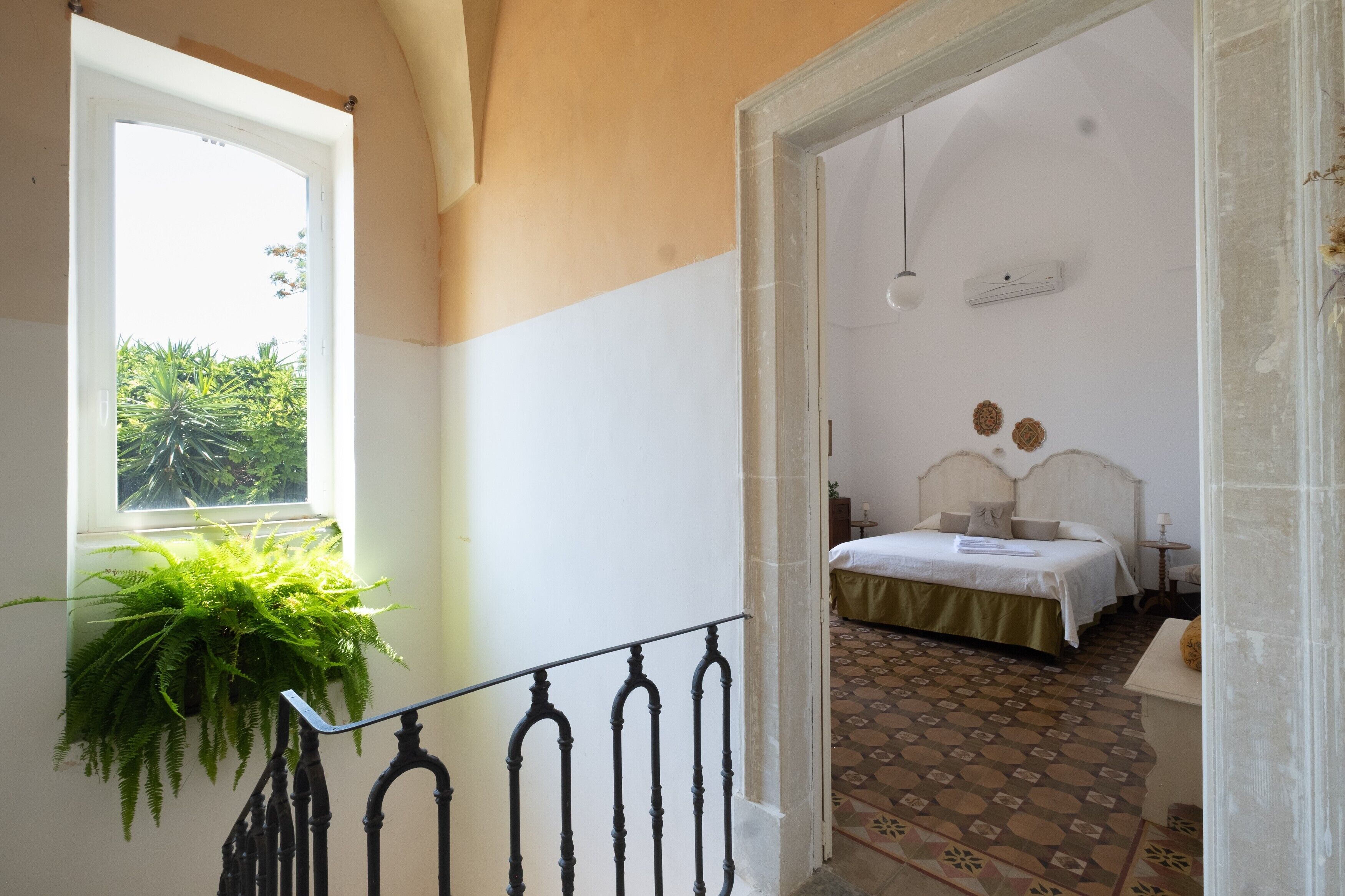 A room with a bed, a window with a plant, and a patterned floor.