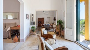 Amplia sala de estar con mesa y sillas de comedor, además de un sofá. Hay una puerta que da a un balcón con plantas.