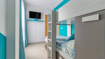 A bedroom with bunk beds, a TV mounted on the wall, and a window with curtains.