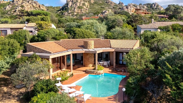 Eine Villa mit Swimmingpool, Sitzgelegenheit im Freien und Blick auf felsige Hügel.