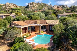 En villa med pool, utomhusmöbler och utsikt över ett kuperat landskap med berg.